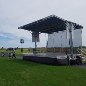 A stage with an open top and a person walking on the grass.