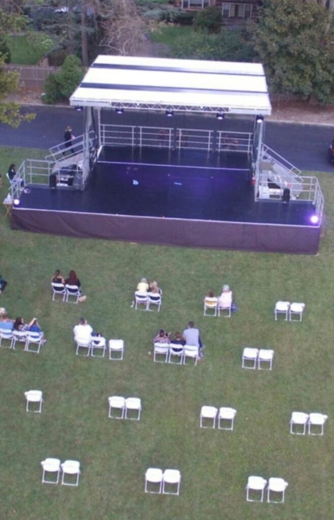An outdoor live event stage with an open top and a person walking on the grass to rent in Long Island and Tri state area from Allseasonsstagerentals.com